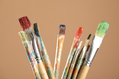 Photo of Dirty paintbrushes on light brown background, closeup