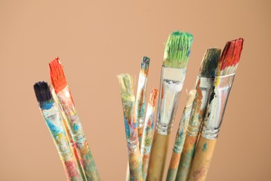 Photo of Dirty paintbrushes on light brown background, closeup