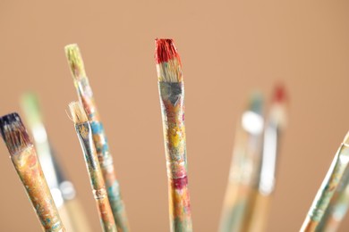 Photo of Dirty paintbrushes on light brown background, closeup