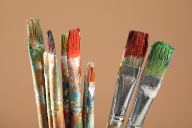 Photo of Dirty paintbrushes on light brown background, closeup