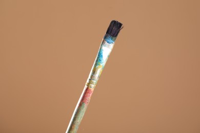 Photo of Dirty paintbrush on light brown background, closeup