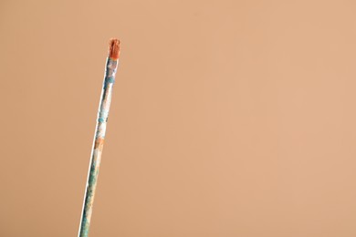Photo of Dirty paintbrush on light brown background, closeup. Space for text