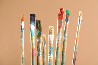 Photo of Dirty paintbrushes on light brown background, closeup
