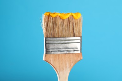 Photo of Brush with yellow paint on light blue background, closeup