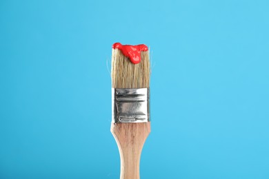 Photo of Brush with red paint on light blue background, closeup
