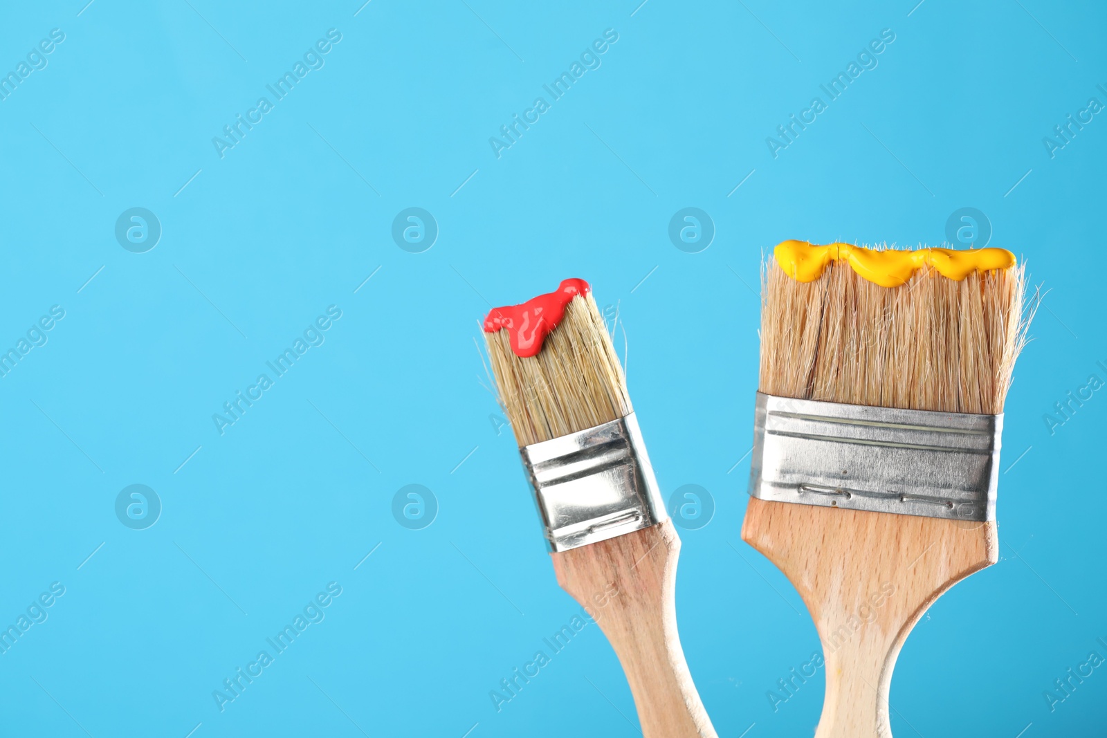 Two brushes with color paints on light blue background, closeup. Space for text Photo of Two brushes with color paints on light blue background, closeup. Space for text
