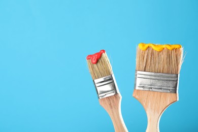 Photo of Two brushes with color paints on light blue background, closeup. Space for text
