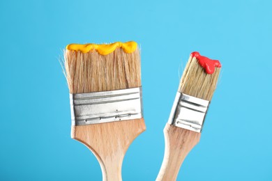 Photo of Two brushes with color paints on light blue background, closeup