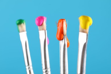 Photo of Many brushes with color paints on light blue background, closeup