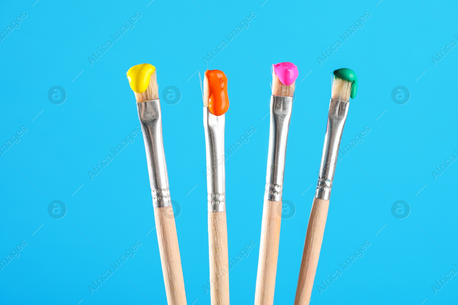 Many brushes with color paints on light blue background, closeup Photo of Many brushes with color paints on light blue background, closeup