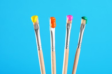 Photo of Many brushes with color paints on light blue background, closeup