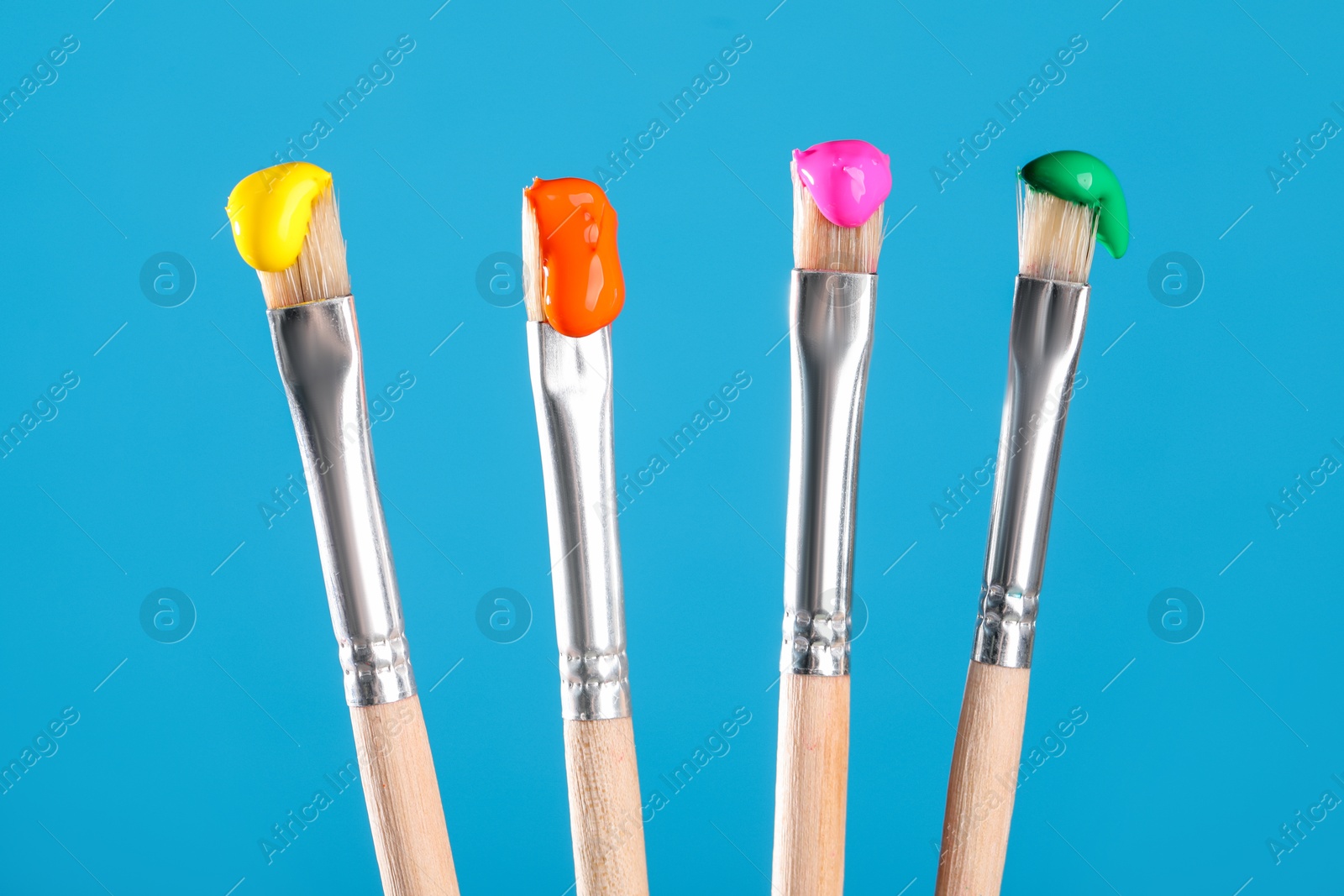 Many brushes with color paints on light blue background, closeup Photo of Many brushes with color paints on light blue background, closeup