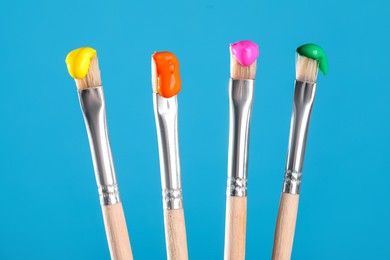 Photo of Many brushes with color paints on light blue background, closeup