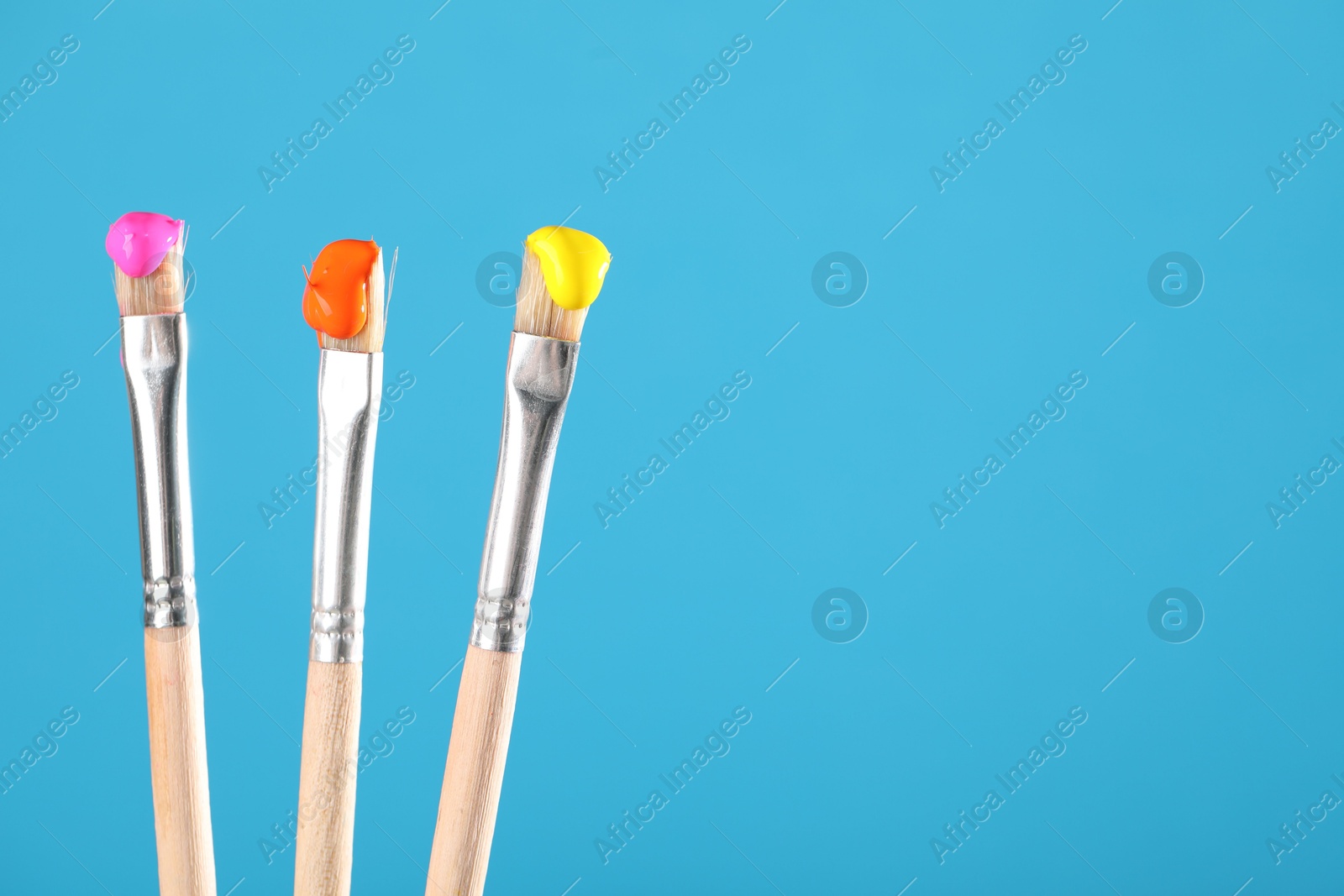 Three brushes with color paints on light blue background, closeup. Space for text Photo of Three brushes with color paints on light blue background, closeup. Space for text