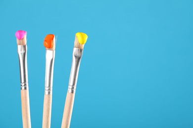 Photo of Three brushes with color paints on light blue background, closeup. Space for text