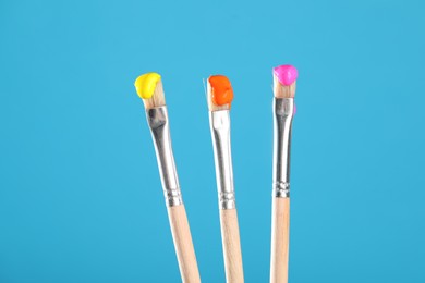 Photo of Three brushes with color paints on light blue background, closeup
