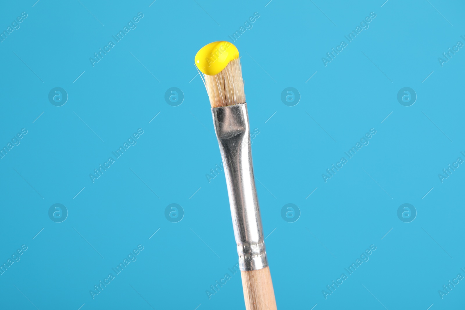 Brush with yellow paint on light blue background, closeup Photo of Brush with yellow paint on light blue background, closeup