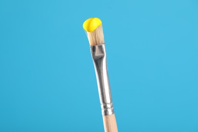 Photo of Brush with yellow paint on light blue background, closeup