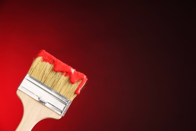 Photo of Brush with paint on red background, closeup. Space for text