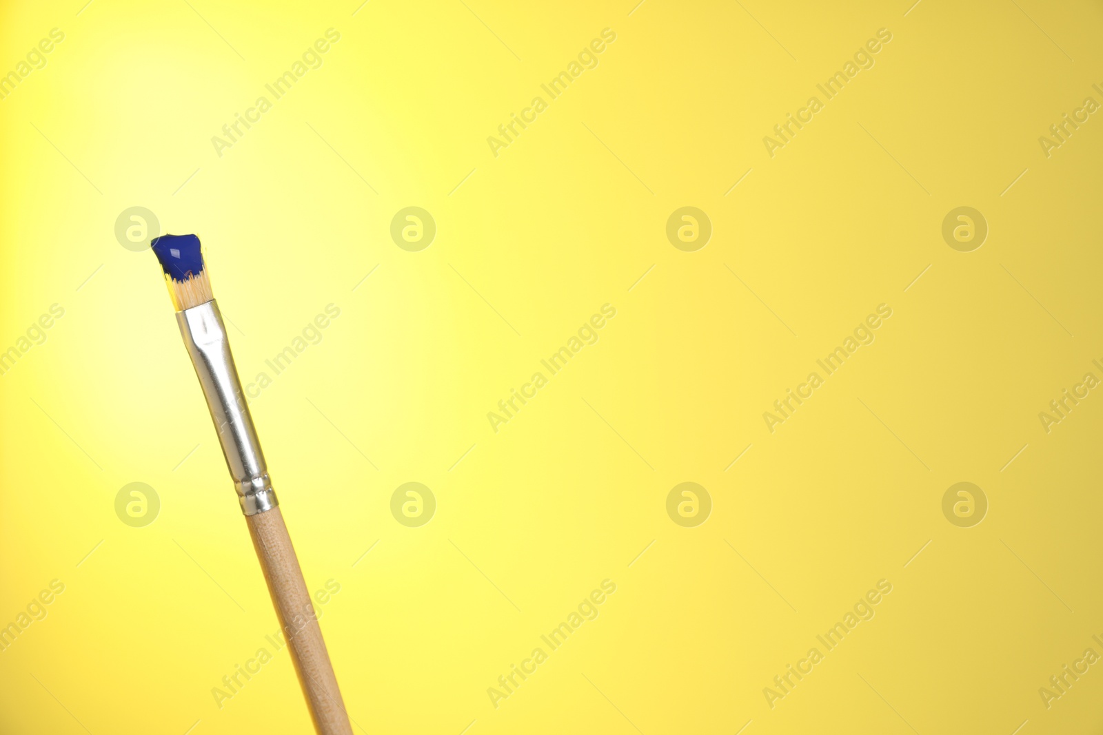Brush with blue paint on yellow background, closeup. Space for text Photo of Brush with blue paint on yellow background, closeup. Space for text