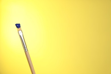Photo of Brush with blue paint on yellow background, closeup. Space for text