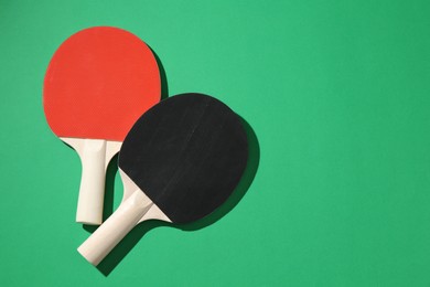 Photo of Ping pong rackets on green background, top view. Space for text