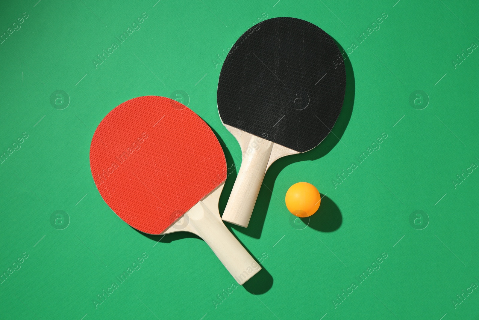 Ping pong rackets and ball on green background, flat lay Photo of Ping pong rackets and ball on green background, flat lay