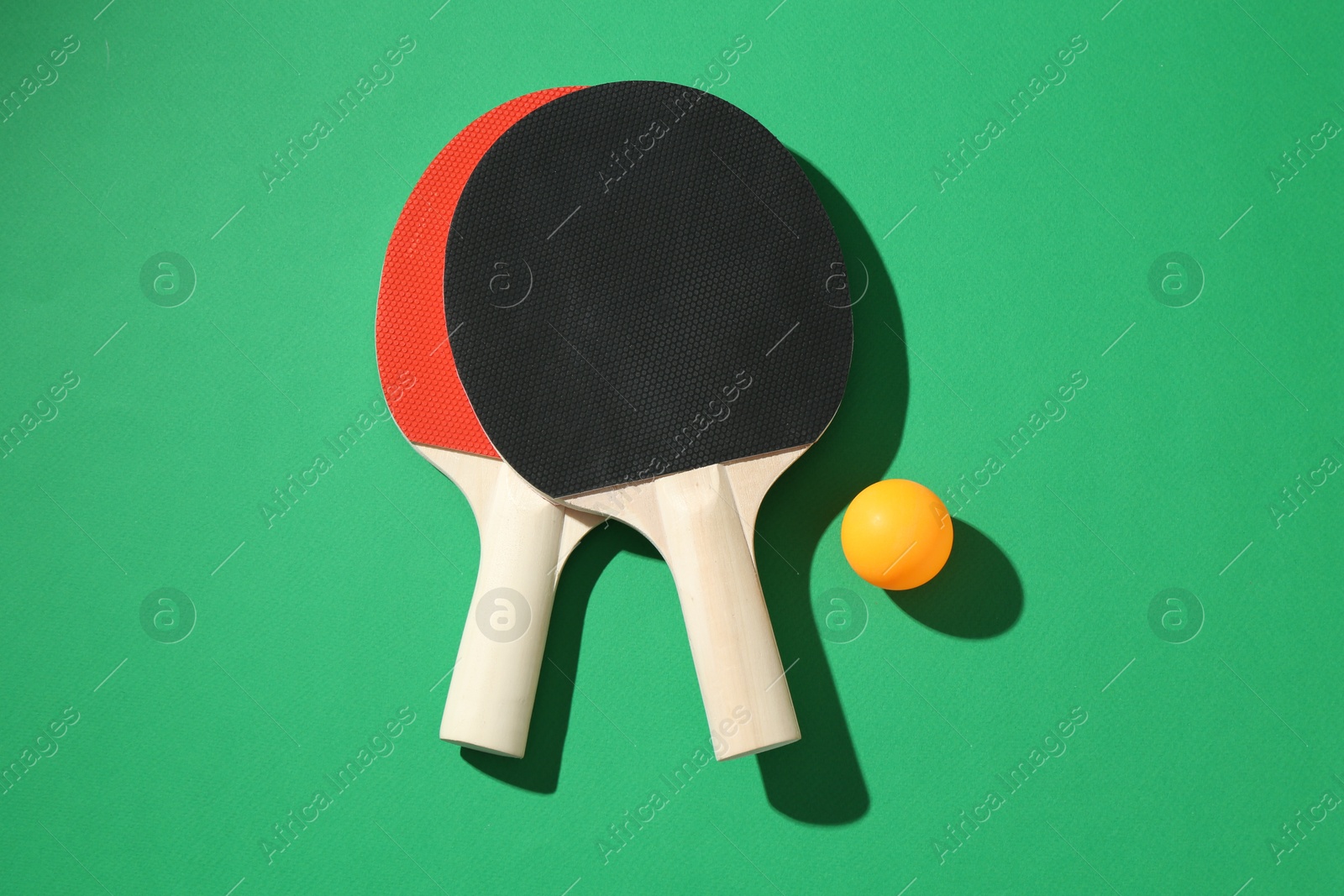 Ping pong rackets and ball on green background, flat lay Photo of Ping pong rackets and ball on green background, flat lay