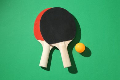 Photo of Ping pong rackets and ball on green background, flat lay