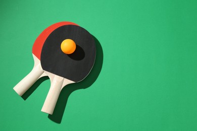 Photo of Ping pong rackets and ball on green background, flat lay. Space for text