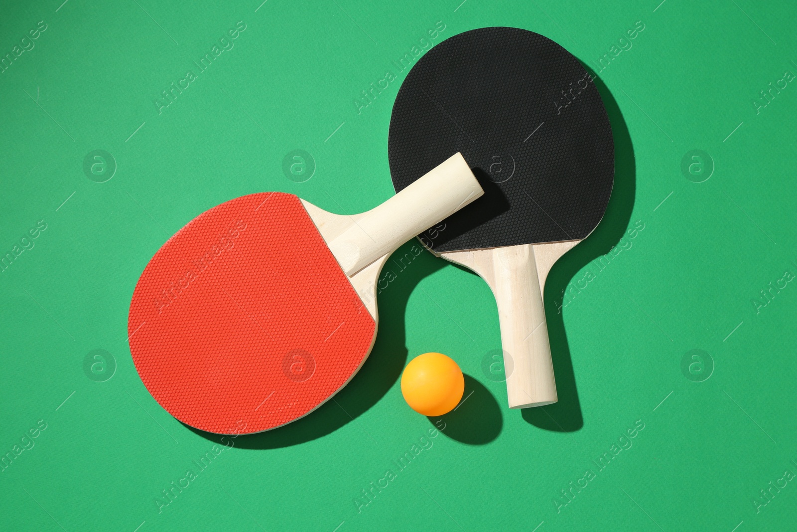 Ping pong rackets and ball on green background, flat lay Photo of Ping pong rackets and ball on green background, flat lay