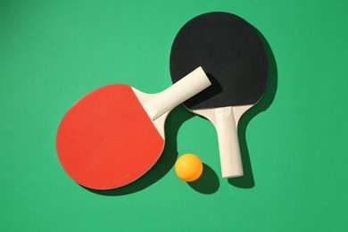 Photo of Ping pong rackets and ball on green background, flat lay