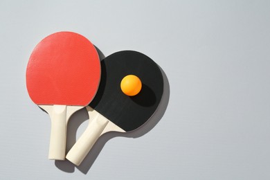 Photo of Ping pong rackets and ball on light background, top view. Space for text