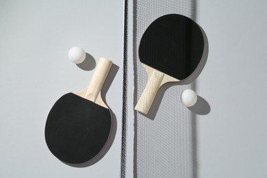 Photo of Ping pong rackets, balls and net on light background, flat lay