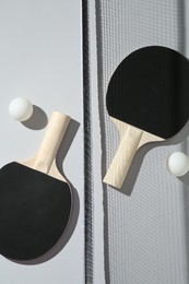 Photo of Ping pong rackets, balls and net on light background, flat lay