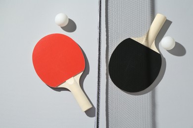 Photo of Ping pong rackets, balls and net on light background, flat lay
