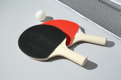 Photo of Ping pong rackets, ball and net on light background