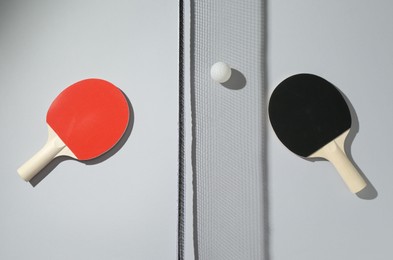 Photo of Ping pong rackets, ball and net on light background, flat lay