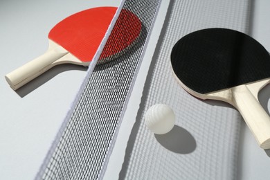 Photo of Ping pong rackets, ball and net on light background