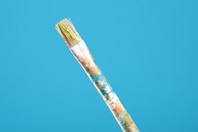 Photo of Dirty paintbrush on light blue background, closeup
