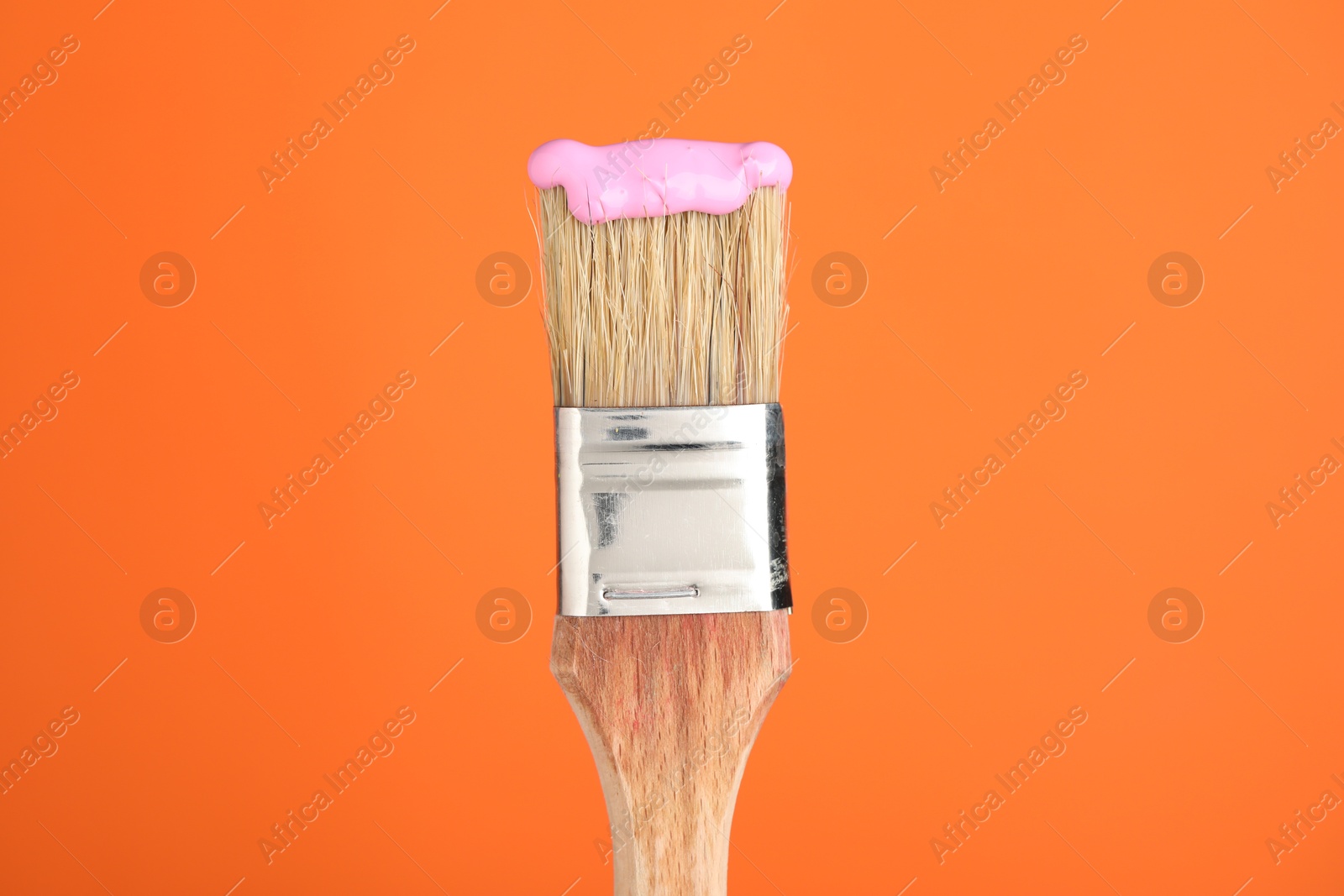 Brush with pink paint on orange background, closeup Photo of Brush with pink paint on orange background, closeup