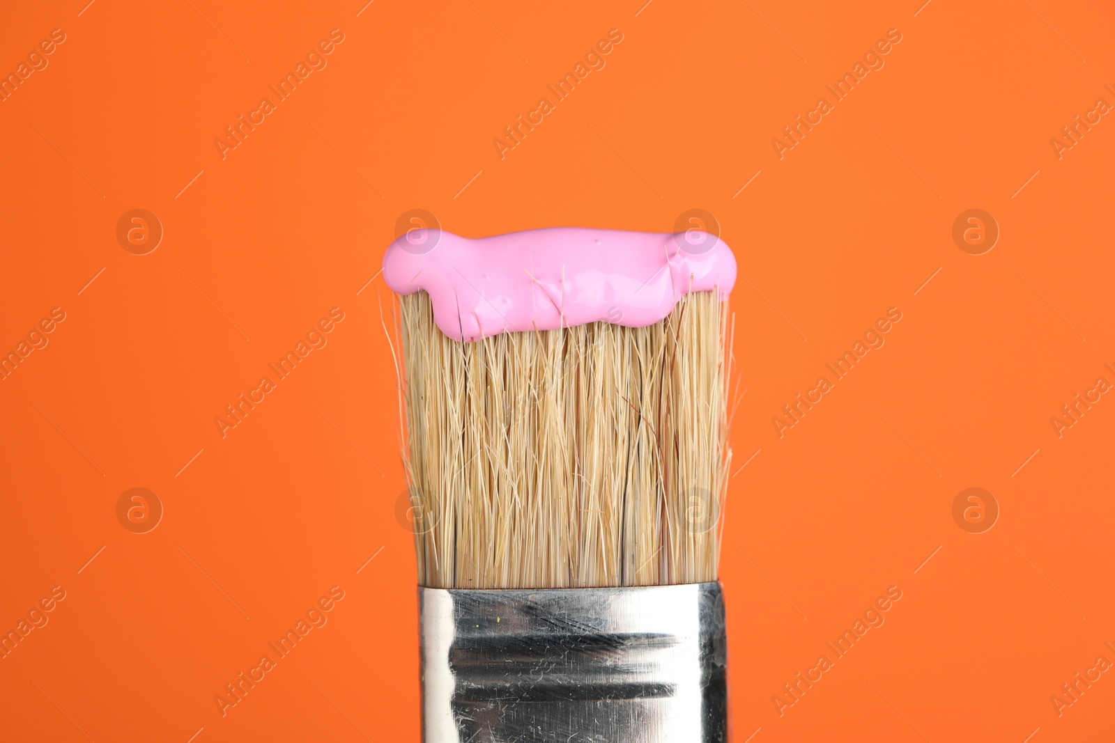 Brush with pink paint on orange background, closeup Photo of Brush with pink paint on orange background, closeup