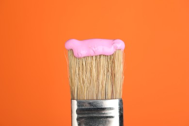 Photo of Brush with pink paint on orange background, closeup