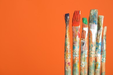 Photo of Many dirty paintbrushes on orange background, closeup. Space for text