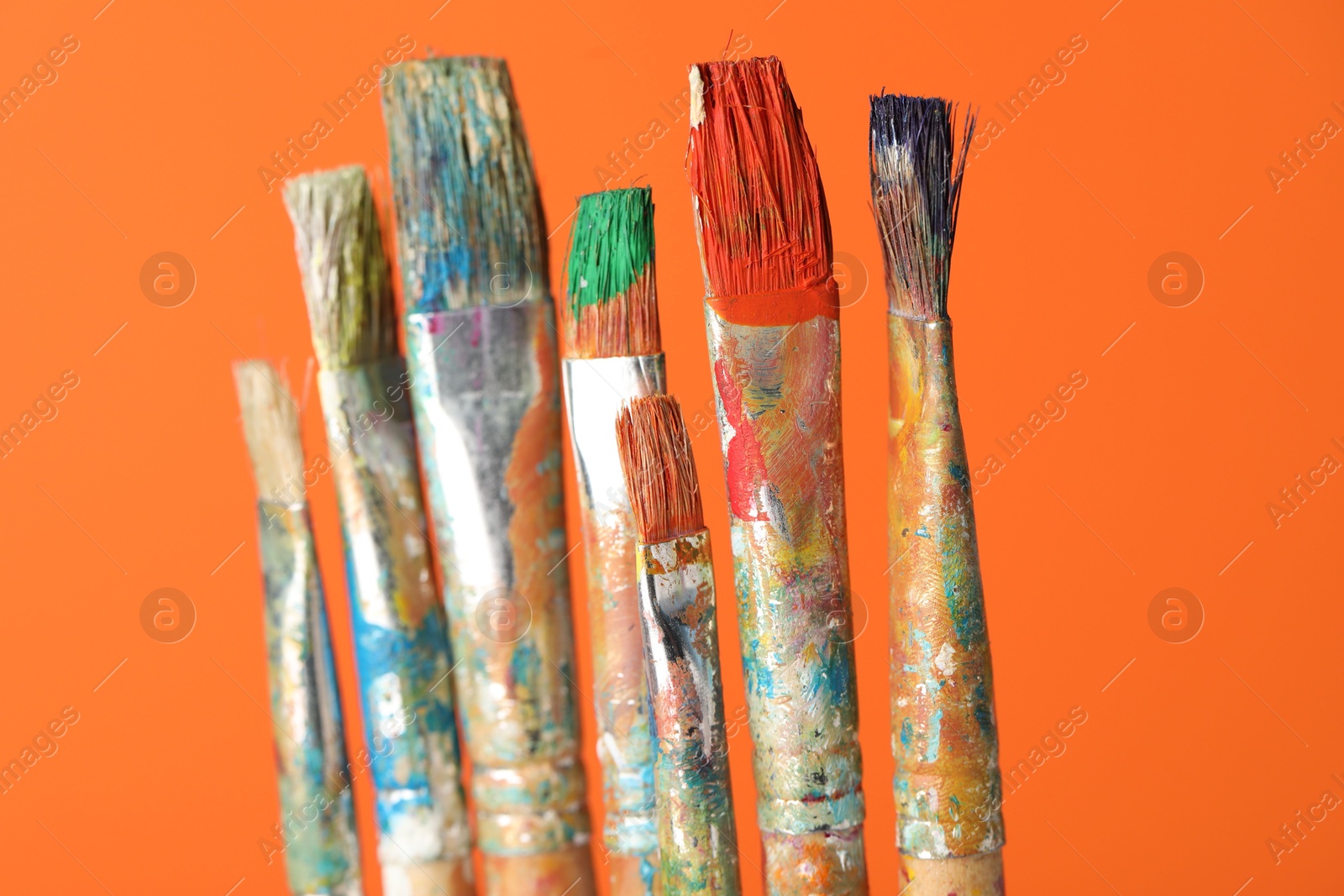 Many dirty paintbrushes on orange background, closeup Photo of Many dirty paintbrushes on orange background, closeup