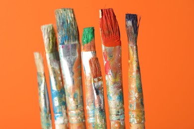 Photo of Many dirty paintbrushes on orange background, closeup