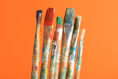 Photo of Many dirty paintbrushes on orange background, closeup