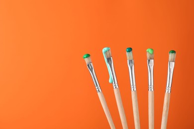 Photo of Many brushes with color paints on orange background, closeup. Space for text