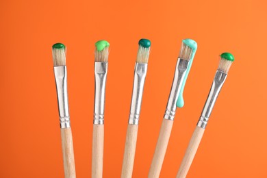 Photo of Many brushes with color paints on orange background, closeup
