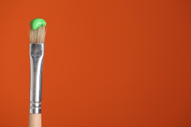 Photo of Brush with green paint on orange background, closeup. Space for text